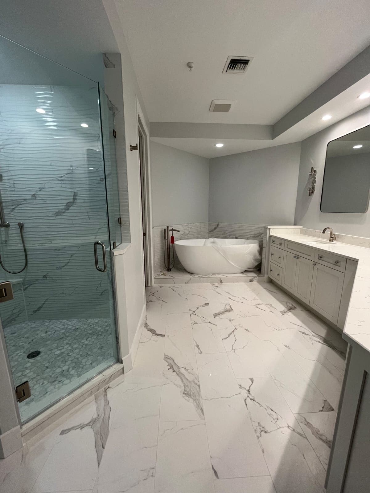 Primary bathroom with glass walk-in shower, freestanding tub and marble-look tile floor