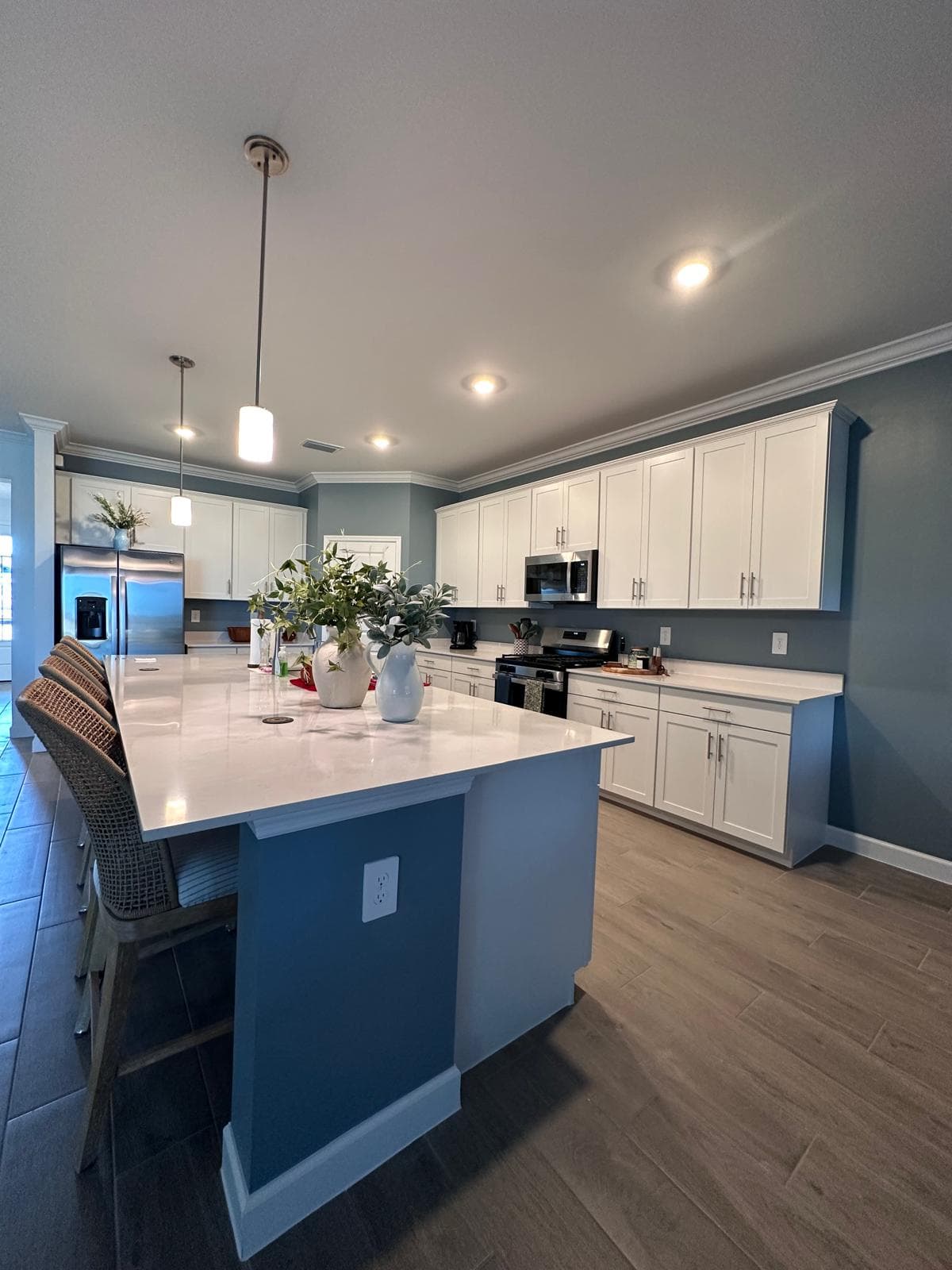White shaker-cabinet kitchen with a large quartz island, pendant lights and crown molding