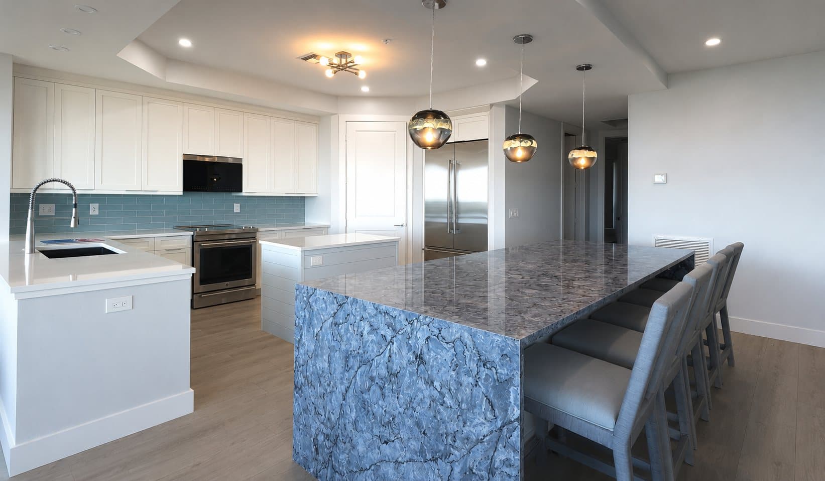 White kitchen with a large waterfall-edge stone island and pendant lights