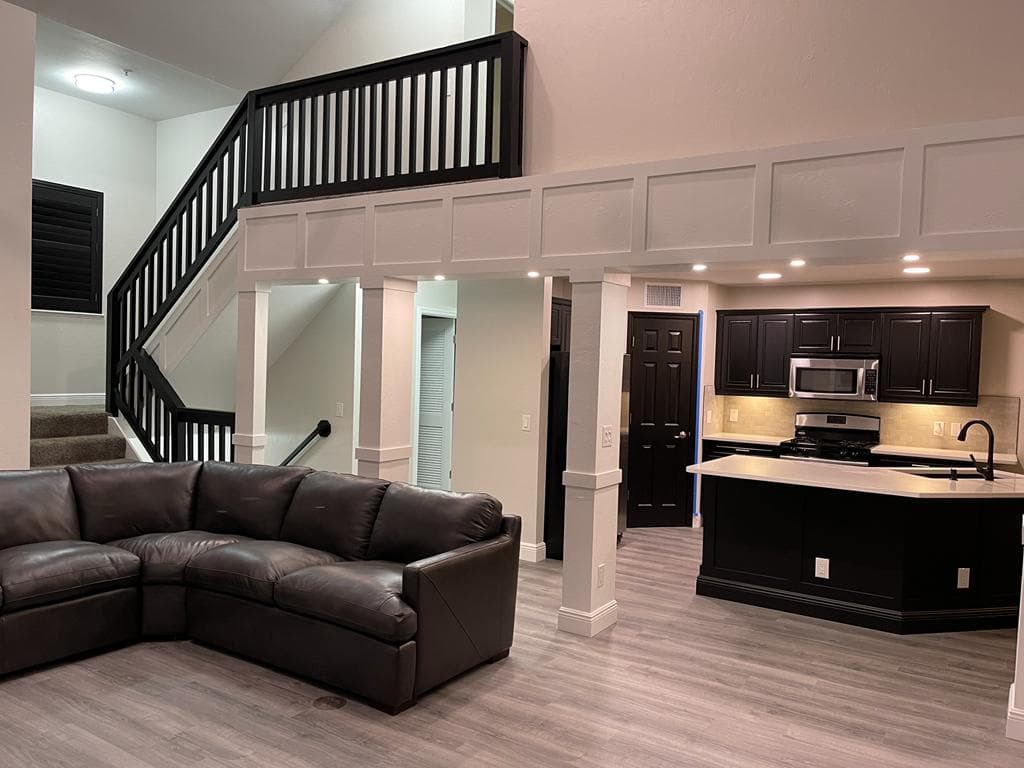 Open living area with a custom paneled beam, staircase railing and kitchen